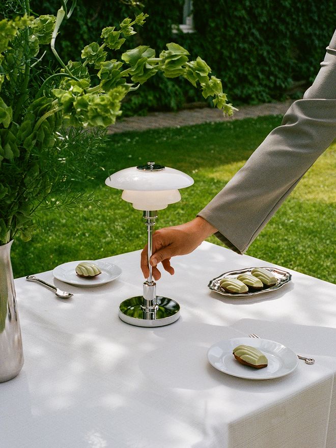 A hand holding a Louis Poulsen lamp outdoors