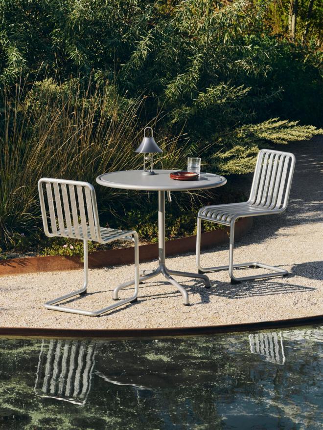 A picture of a summer landscape by the water with Palissade Cantilever chairs arranged around a round garden table