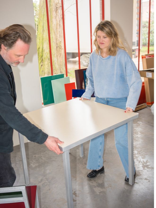 Hannes Van Severen and Fien Muller carrying a white Alu table in their studio