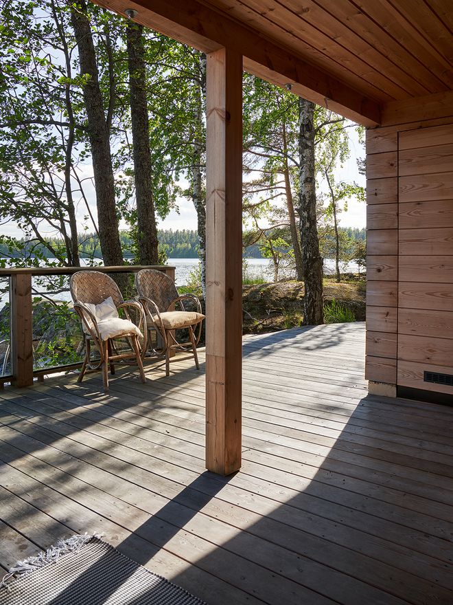 The cabin's terrace wraps around the entire building, with Lake Saimaa and a conifer forest in the background.