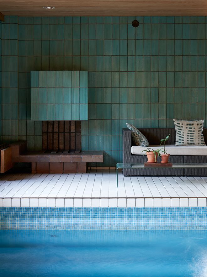 A tiled fireplace next to swimming pool indoors.