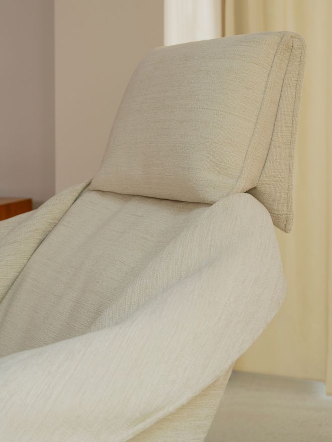 Close-up of a lounge chair whose off-white fabric cover falls in soft folds over the backrest.