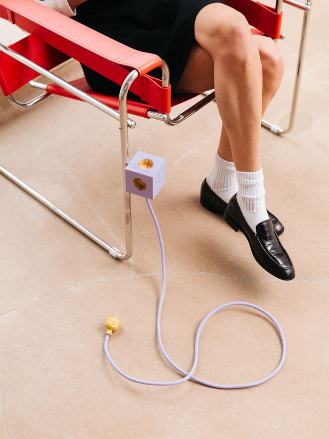 Woman sitting on a red chair with Avolt's Square 1 extension cord attached on the steel leg