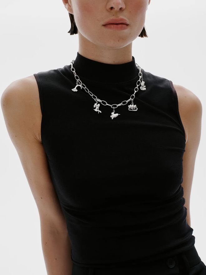 A person in a black sleeveless top wearing a silver chain necklace adorned with several small flower charms