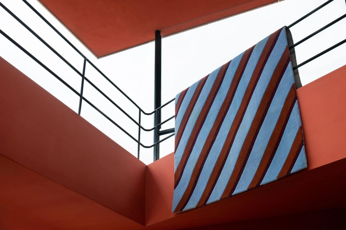 LAYERED’s striped Teklan Diagonal wool rug airing on a balcony railing