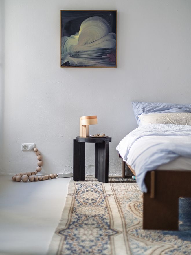 The black-stained Vaarnii 001 stool used as a bedside table in the bedroom