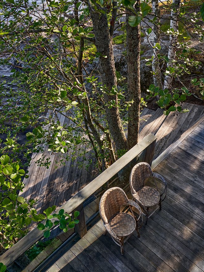 A wooden dock on the shores of Lake Saimaa, extending from the cabin's lower terrace, surrounded by birches and other vegetation.