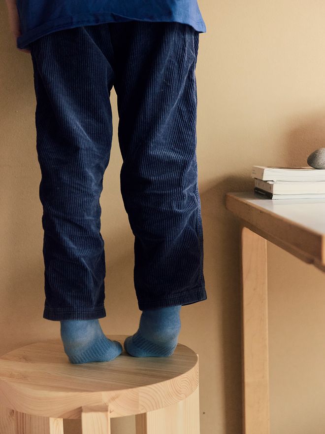 Vaarnii 001 stool in pine, a child standing on a stool with dark blue corduroy pants, cropped image with only legs visible