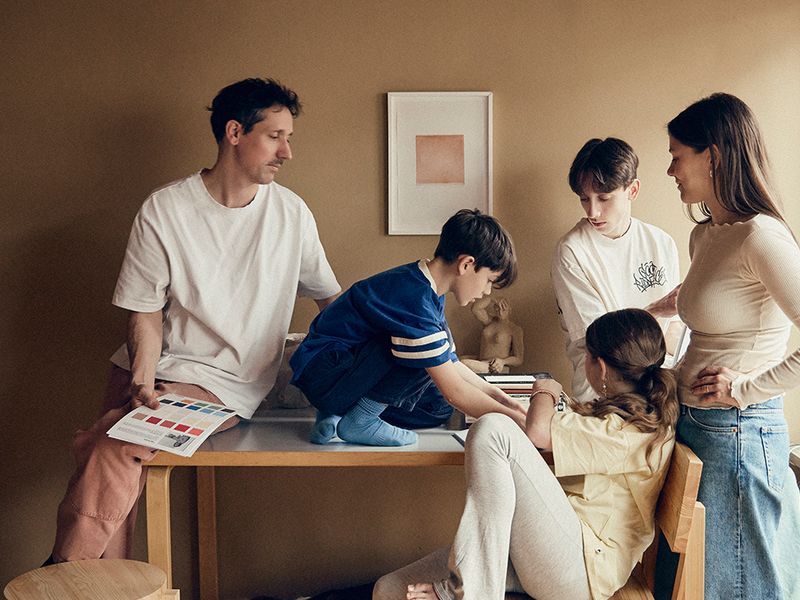 Ida Lauda with her partner and children sitting and standing around an Artek table, with Vaarnii 001 stool and 001 dining chair