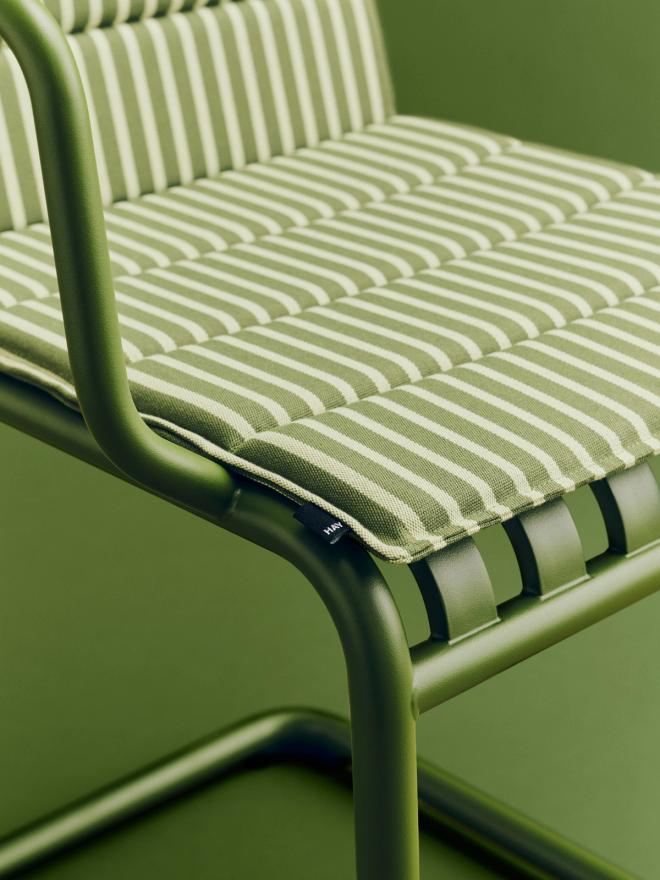 Close-up photo of an olive green Palissade Cantilever chair with a striped seat cushion placed on top