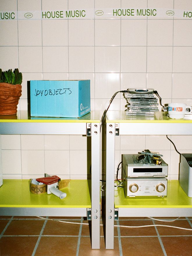Yellow shelves with CDs and stereo equipment against a tiled wall, with 'HOUSE MUSIC' text along the top.