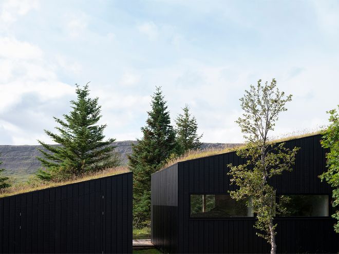 An image of the Holiday home by Þingvallavatn by KRADS architects: a leisure home located in Iceland in the middle of a picturesque scenery. This image features the buildings black facade and a greened roof.