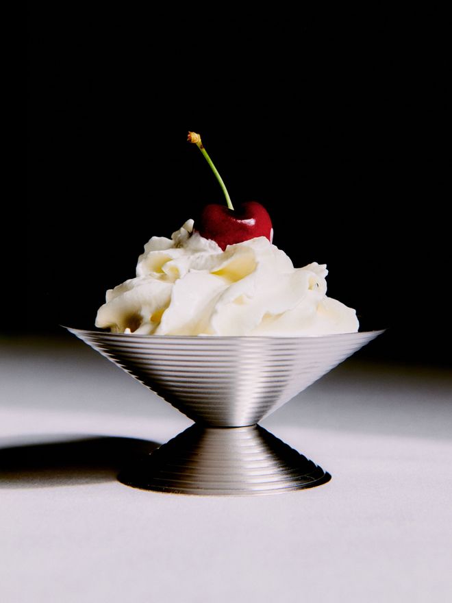 Close-up of Service Projects’ stainless steel Ice Cream cup filled with ice cream and topped with a cherry on a softly styled table setting.