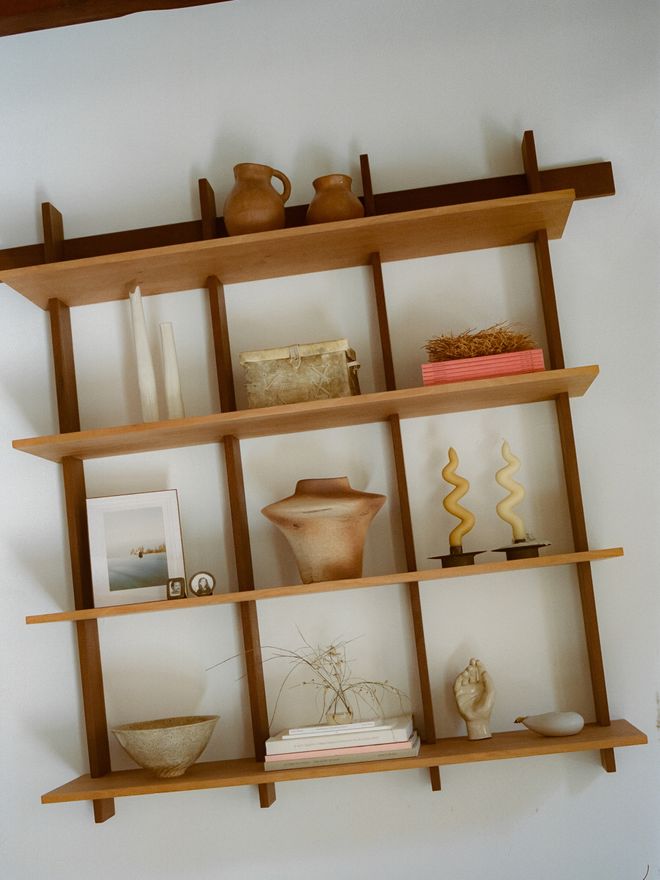 A wooden wall shelf displaying ceramic pieces, books, candleholders, and small decorative objects.