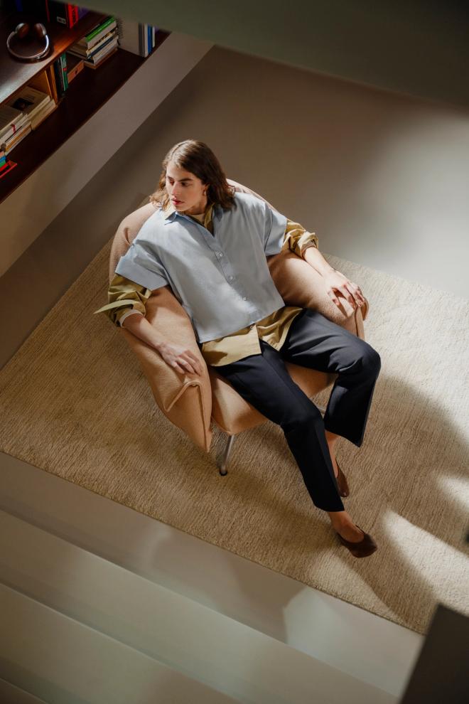 Seen from above, a woman sits in a pale lounge chair with a beige outer cover and a yellow lining.