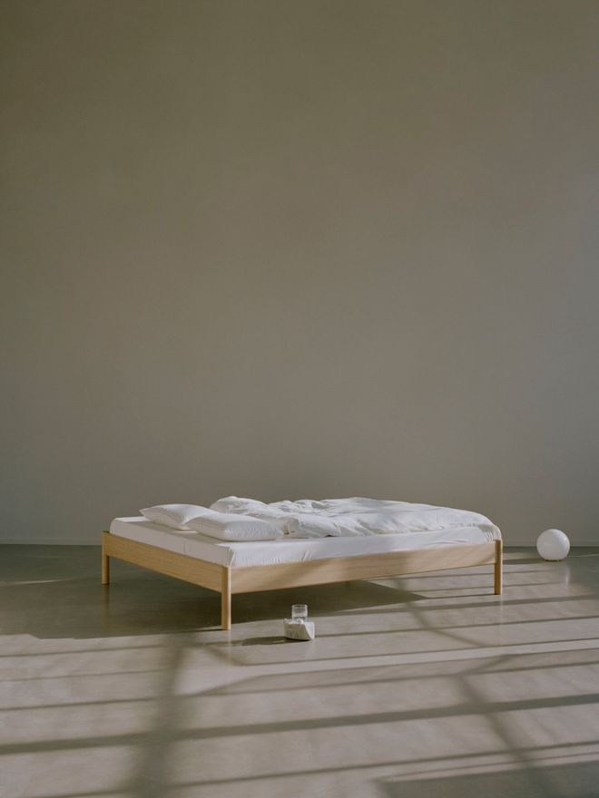 A photo of the bedframe, made up with white sheets, taken in a neutral and spacious setting