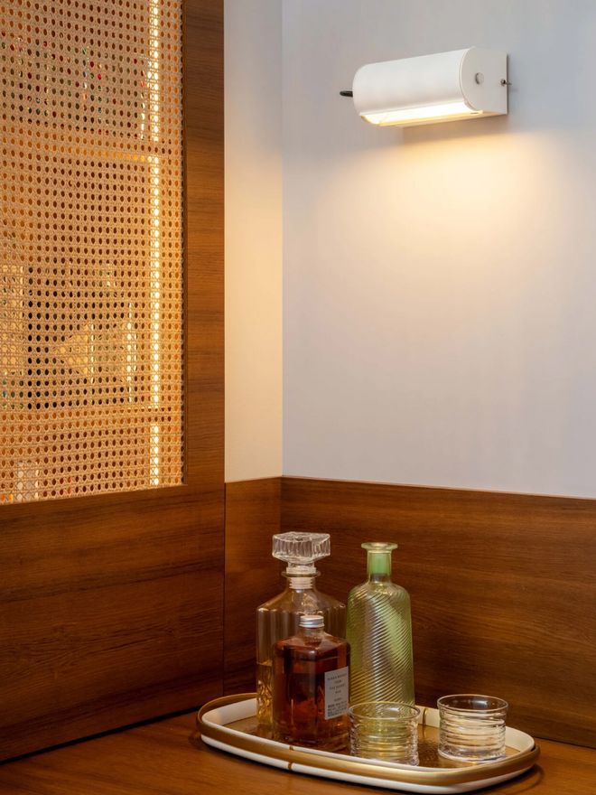 White Applique Cylindrique Petite wall lamp in a wood-paneled corner, above a tray with decanters and glasses.