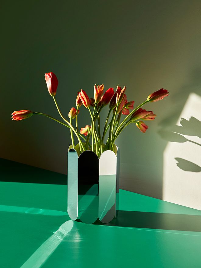 HAY's mirrored Arcs vase filled with tulips, placed on a green table.