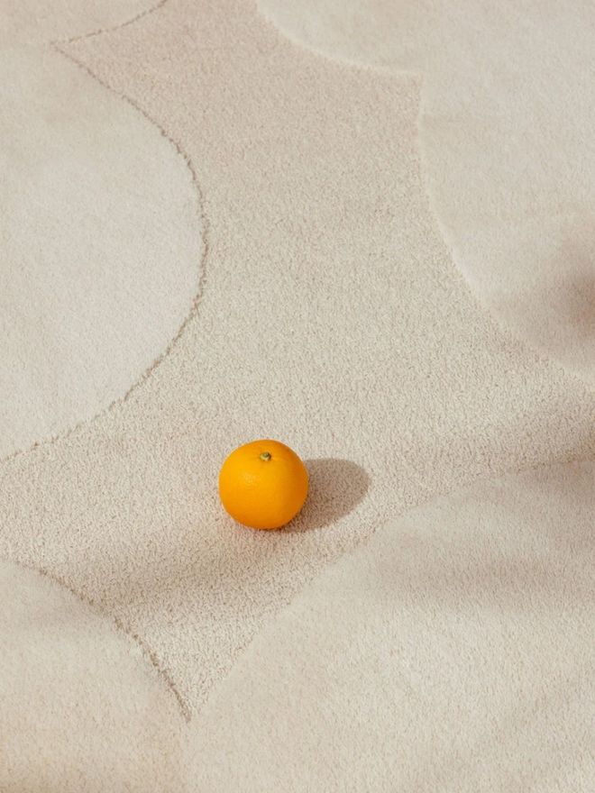 Close-up of a natural white wool rug surface with an orange resting on it