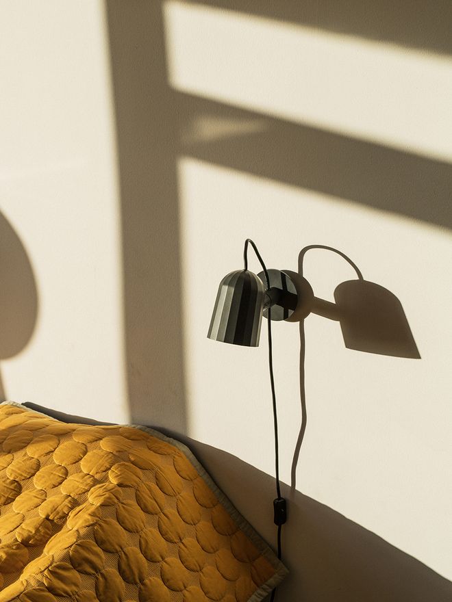 The Noc wall light by Hay in a dark grey color, attached to a bedroom wall.