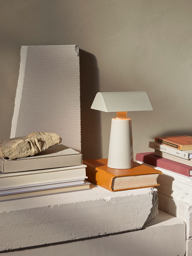 An image of &Tradition's Caret MF1 portable table lamp next to a stack of books.