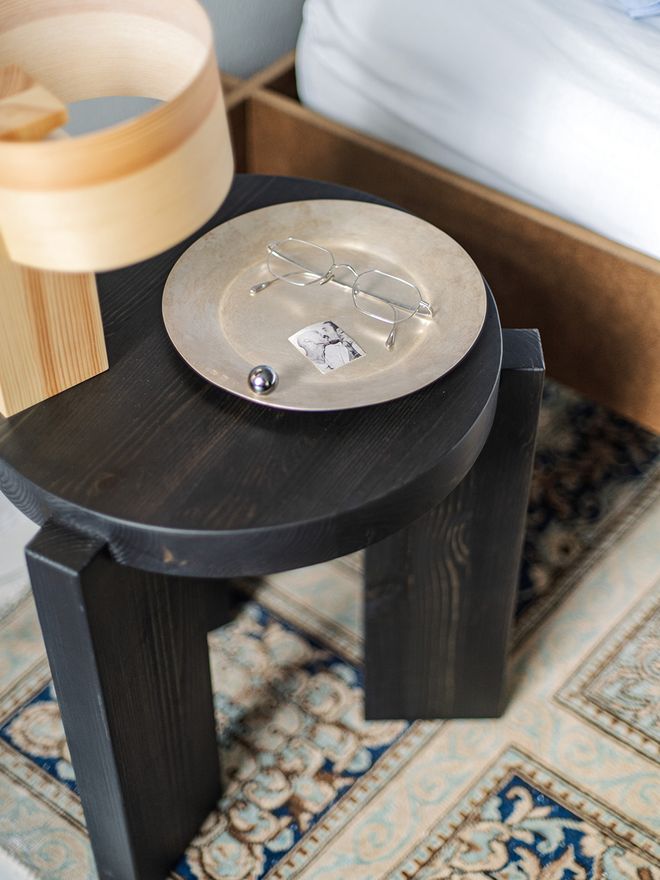 A detail of the Vaarnii 018 Hoop table lamp on the black 001 stool, which holds a tray, eyeglasses, and jewelry