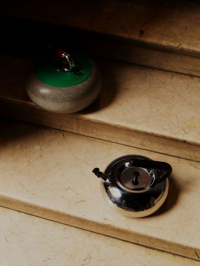 Alessi's Bulbul steel kettle with a curling stone next to it