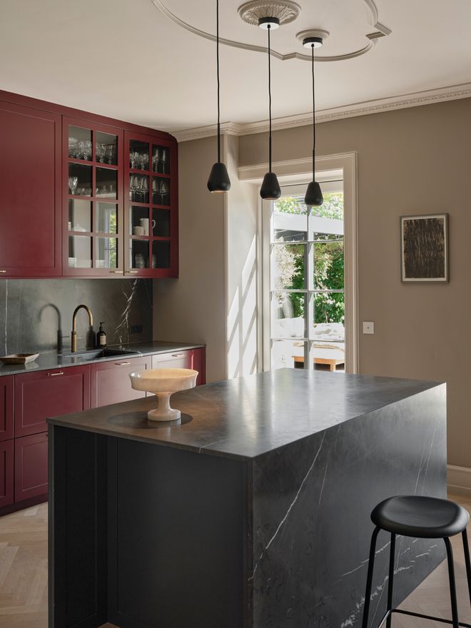 A kitchen with deep red cabinets, a dark marble island, and three black pendants overhead.