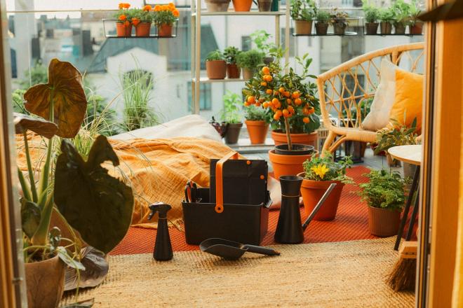 A lush balcony filled with potted plants, orange textiles and gardening tools