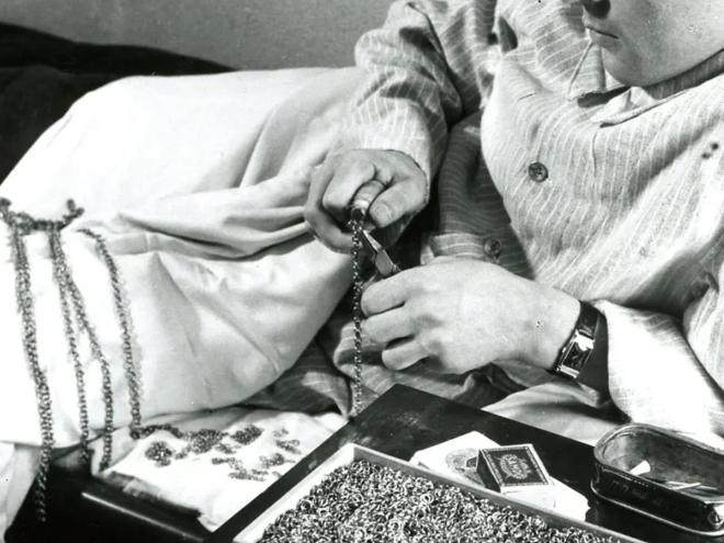 Black-and-white photo of a war veteran making jewellery in bed.