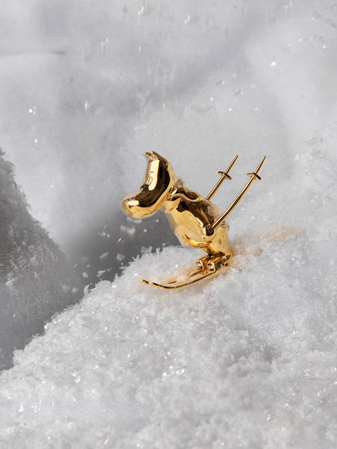 A gilded Moomintroll figurine skiing down a snowy slope.