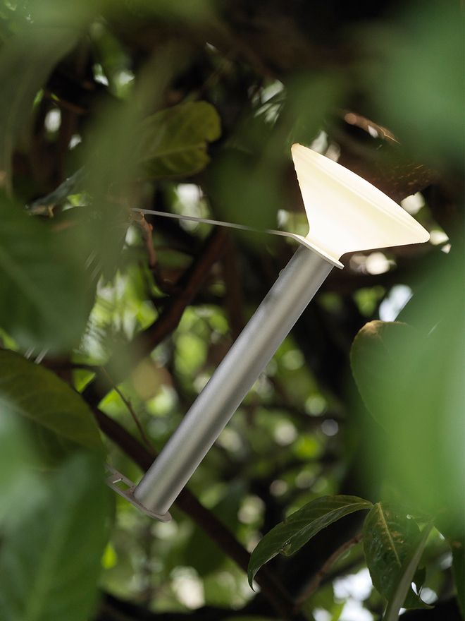 Muuto's portable Piton lamp hung up on a tree branch.