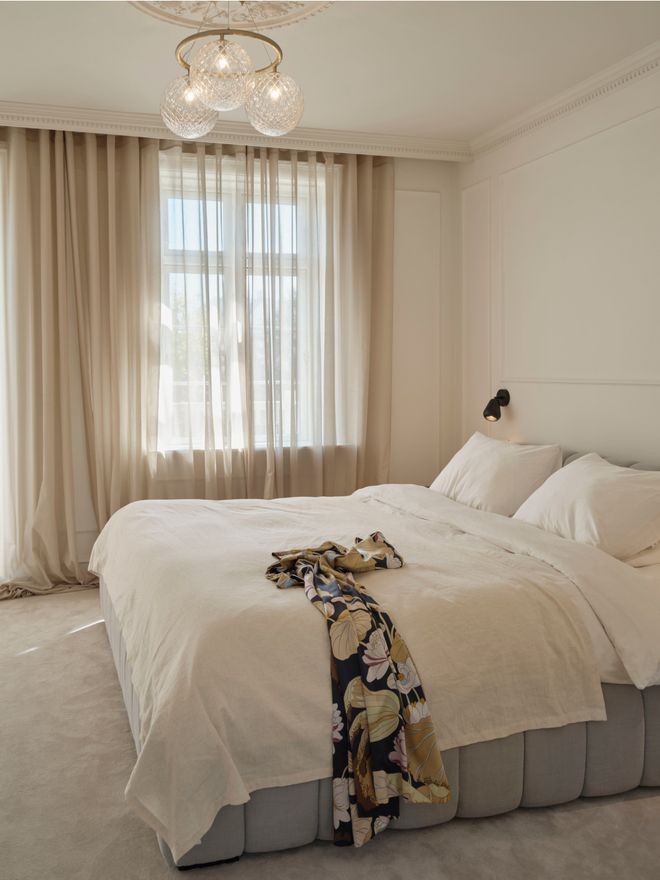 A white double bed and a chandelier in a light bedroom.