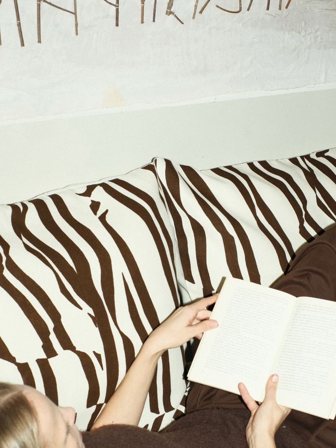 A person relaxing with a book, resting against a black-and-white striped cushion