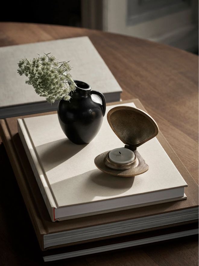 Ferm Living’s brass Clam lantern and a vase on top of a stack of books