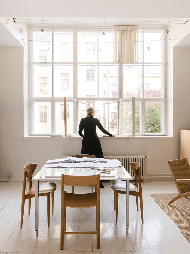 An image of a room with large windows and a work desk with wooden chairs.