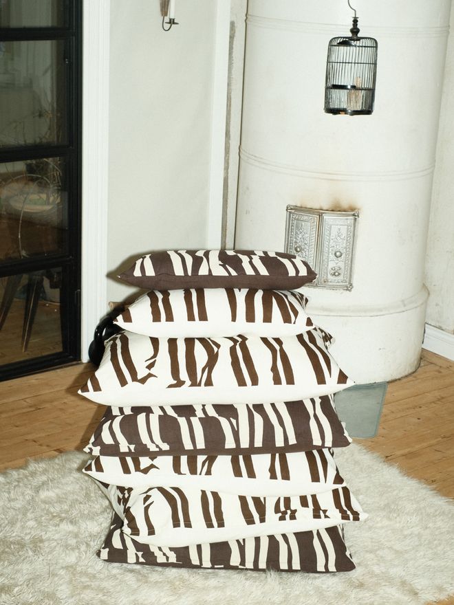 A stack of black-and-white striped cushions on a light shaggy rug, with a white tiled stove and a candle lantern in the background