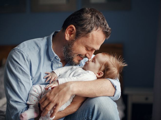 A smiling man holding a baby, touching his nose with the baby's.