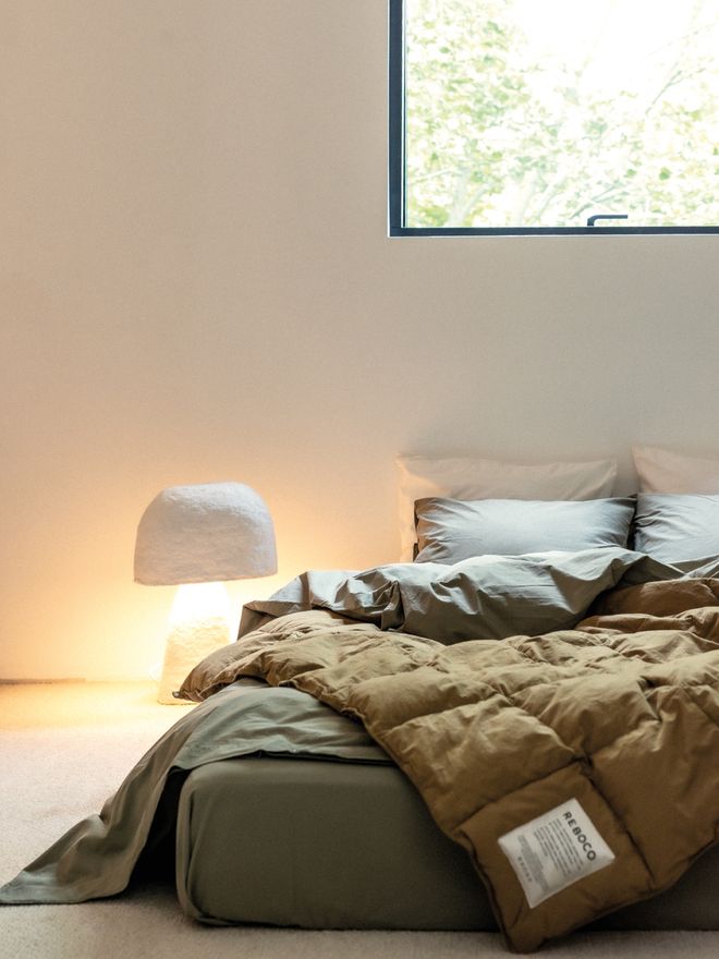 A neatly made bed with Reboco bed linen and a thick, quilted duvet folded over the top.