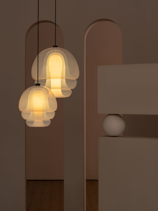 Two lit Medusa glass pendant lamps hang at different heights in a dimly lit room with tall arched doorways