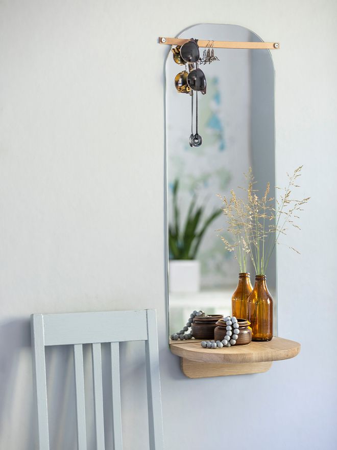 Tapio Anttila's Renki mirror with a brown glass bottle and a small ceramic bowl on the mirror's shelf and sunglasses hanging from the mirror's leather strap.