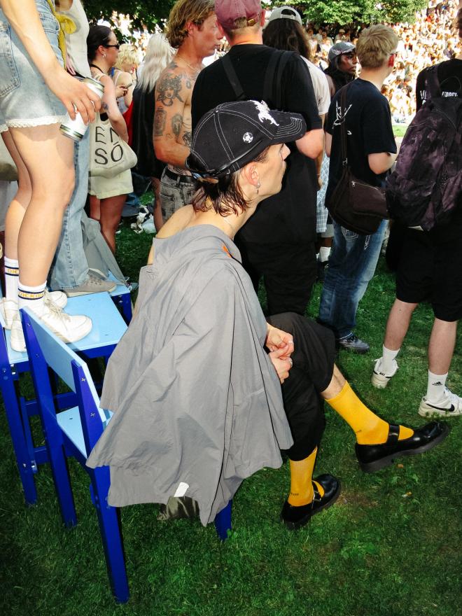 A person sit on a blue chair in a festival crowd.