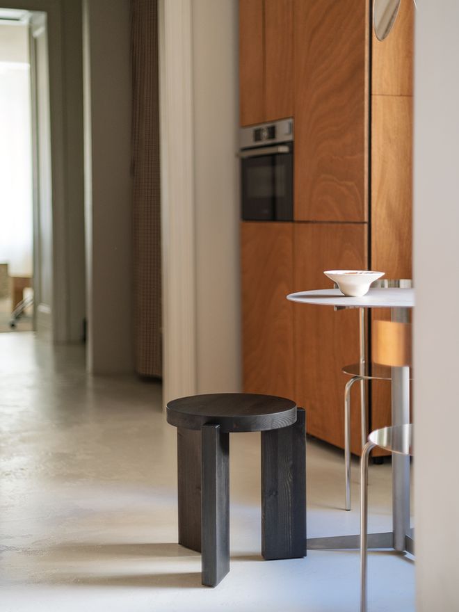 The black-stained Vaarnii 001 stool standing on the concrete floor of the wood-toned kitchen