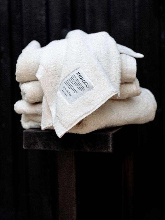 A stack of thick, white Reboco towels folded neatly on a bed, highlighting their plush, hotel-like softness and texture.