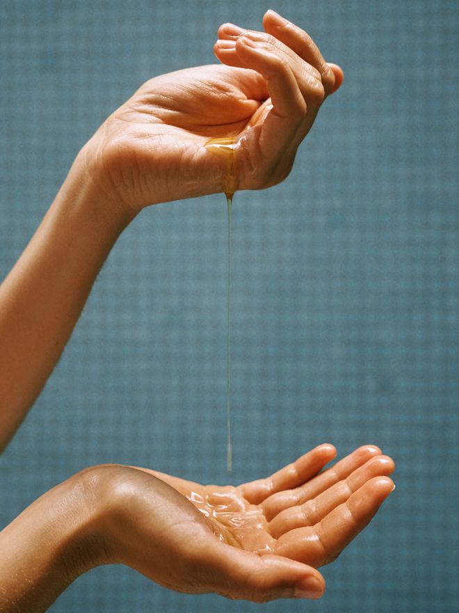 Golden body oil pouring from one hand into another's palm