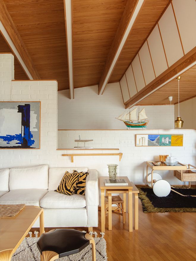 Villa Skeppet's living room with a cream sofa, wooden shelving, and an untitled 1962 painting by Alvar Aalto hanging above the seating area