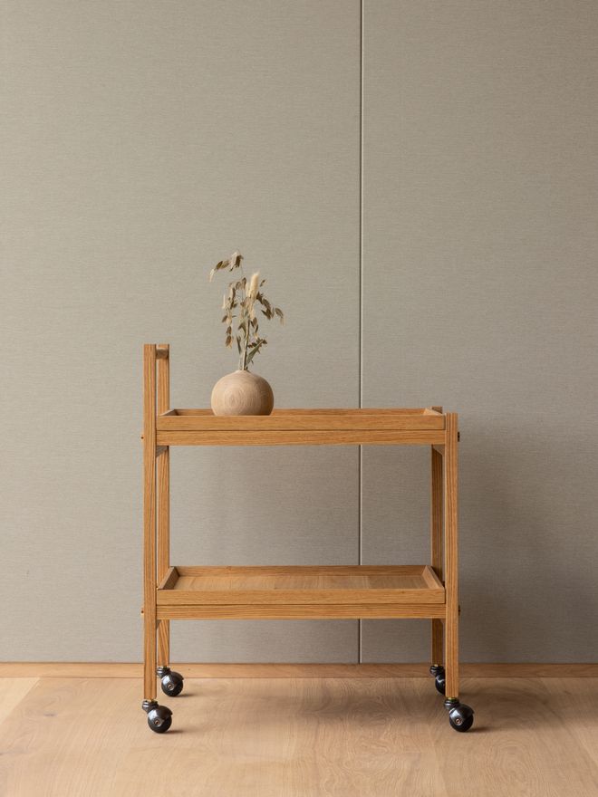 The oak serving trolley with a bouquet of flowers placed on top, styled in a calm, minimalist interior setting.