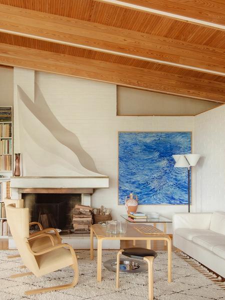 The living room of Villa Skeppet, designed by Alvar Aalto, featuring warm wooden ceiling beams, a sculptural wave-like fireplace, and Artek furniture