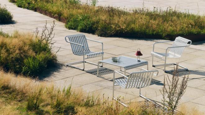 Photo of HAY's silver steel Palissade Cantilever chairs surrounding a matching Palissade garden table in a spacious and green park