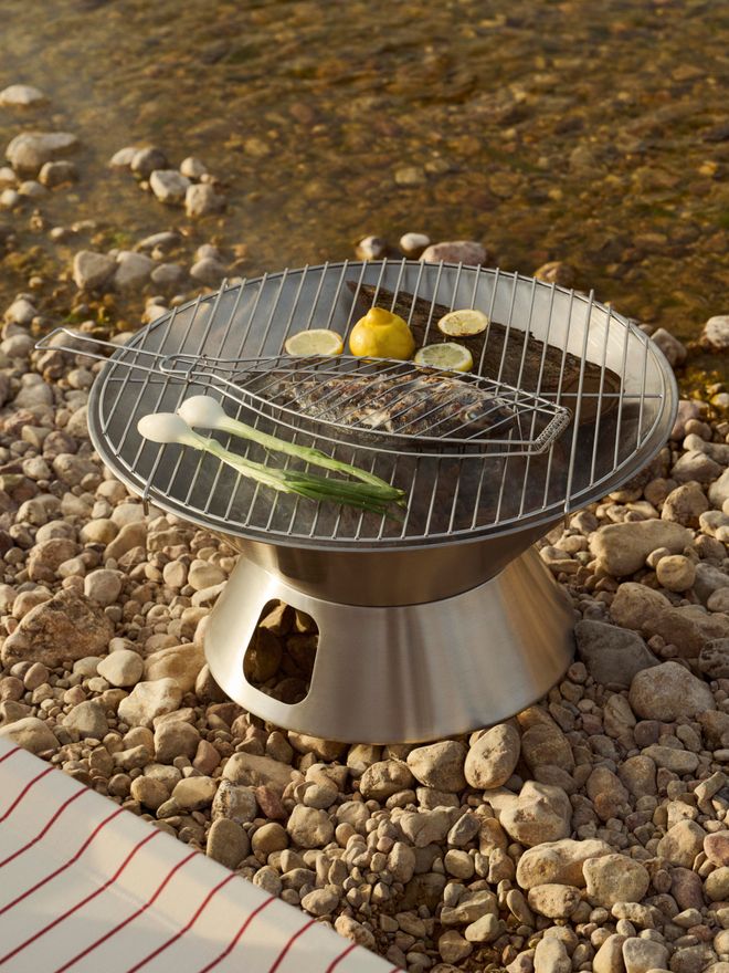 A close-up of the HAY Outdoor Market fire pit, with food placed on the grill grate to cook